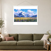 Wildflower Plain Below Snow Peaks, shown as a complete bordered art print with white hanging rods above a sofa in a living room.