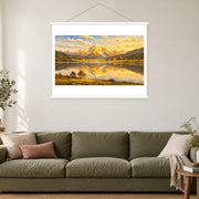 Alpine Village in Golden Reflection, shown as a complete bordered art print with white hanging rods above a sofa in a living room.